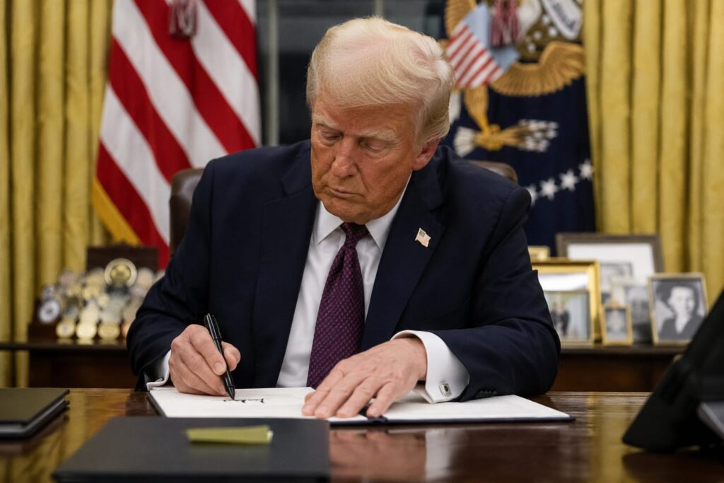 Donald Trump signing official documents in a formal office setting 